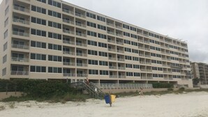 Un hotel de varios pisos con balcones, ubicación frente a la playa y una escalera que conduce a la entrada.
