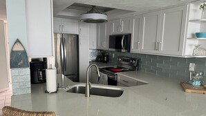 Una cocina moderna con armarios blancos, electrodomésticos de acero inoxidable, una isla grande con un lavamanos y sillas de mimbre.