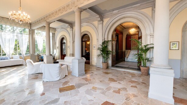 Un hallo espacioso con columnas blancas, suelo de piedra y un candelabro.