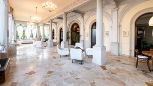 Un vestíbulo amplio con columnas blancas, candelabros y suelo de piedra.