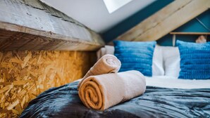A bedroom with a sloped ceiling, wooden wall, and a bed with rolled towels. - Stylish 1BDR Duplex Loft Piccadilly (Manchester)