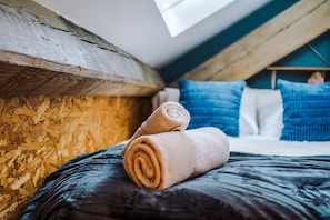 Ein Schlafzimmer mit geneigter Decke, Holzwand und einem Bett mit aufgerollten Handtüchern.