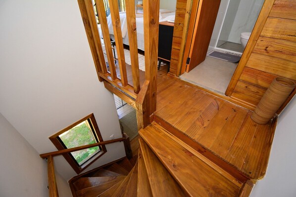 A wooden staircase leading to a bedroom with a bed and a bathroom visible in the background. - Aconchegante Cabana em Sambaqui - NDI013 (Florianópolis)