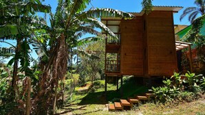 A wooden cabin with a balcony, surrounded by banana trees and greenery. - Aconchegante Cabana em Sambaqui - NDI013 (Florianópolis)