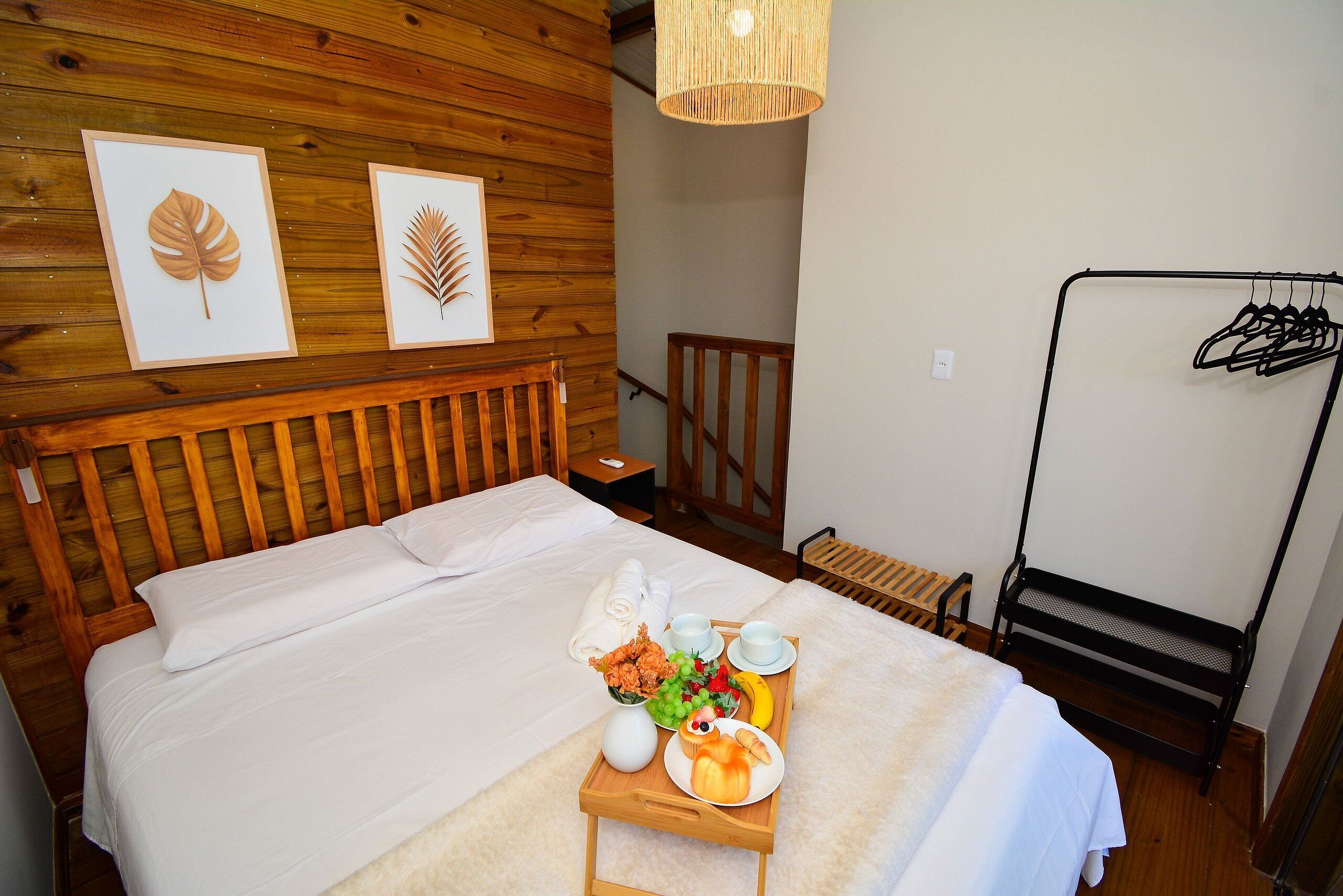 A neatly made bed with a tray of breakfast items, wooden headboard, and two framed leaves on the wall.