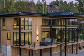 A modern two-story house with large windows, a deck, and a stone chimney.