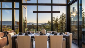 A dining area with a table set for six, large windows, and a view of a forested landscape. - The Edge - Modern Retreat with Panoramic Views (Sandpoint)