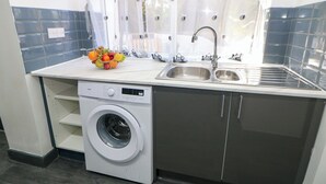 A compact kitchen with a washing machine, a sink, and a fruit bowl on the countertop. - Potter's Wheel (Stoke-on-Trent)