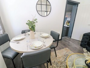 A dining area with a round table set for four, surrounded by chairs, a vase with greenery, and a mirror on the wall. - Potter's Wheel (Stoke-on-Trent)