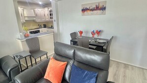 A living area with a sofa, a dining table with chairs, and a kitchen in the background. - Bright 2-Bed Apt with Balcony in Zone 2 London, 3min walk from MaidaVale tubestn (London)