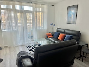 Ein Wohnzimmer mit einem schwarzen Ledersofa, einem Glastisch und einem schwarzen Sessel.