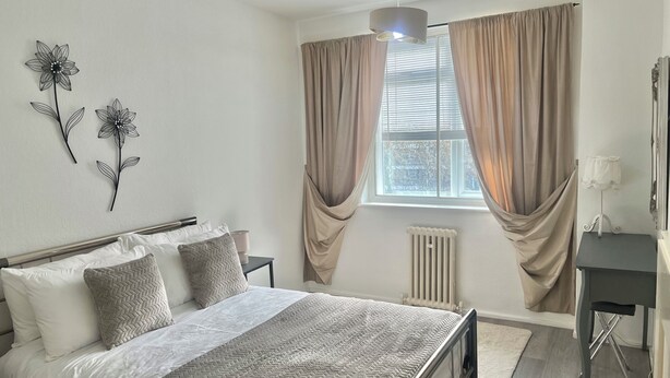 A bedroom with a bed, bedside tables, a radiator, and a window with curtains. - Bright 2-Bed Apt with Balcony in Zone 2 London, 3min walk from MaidaVale tubestn (London)