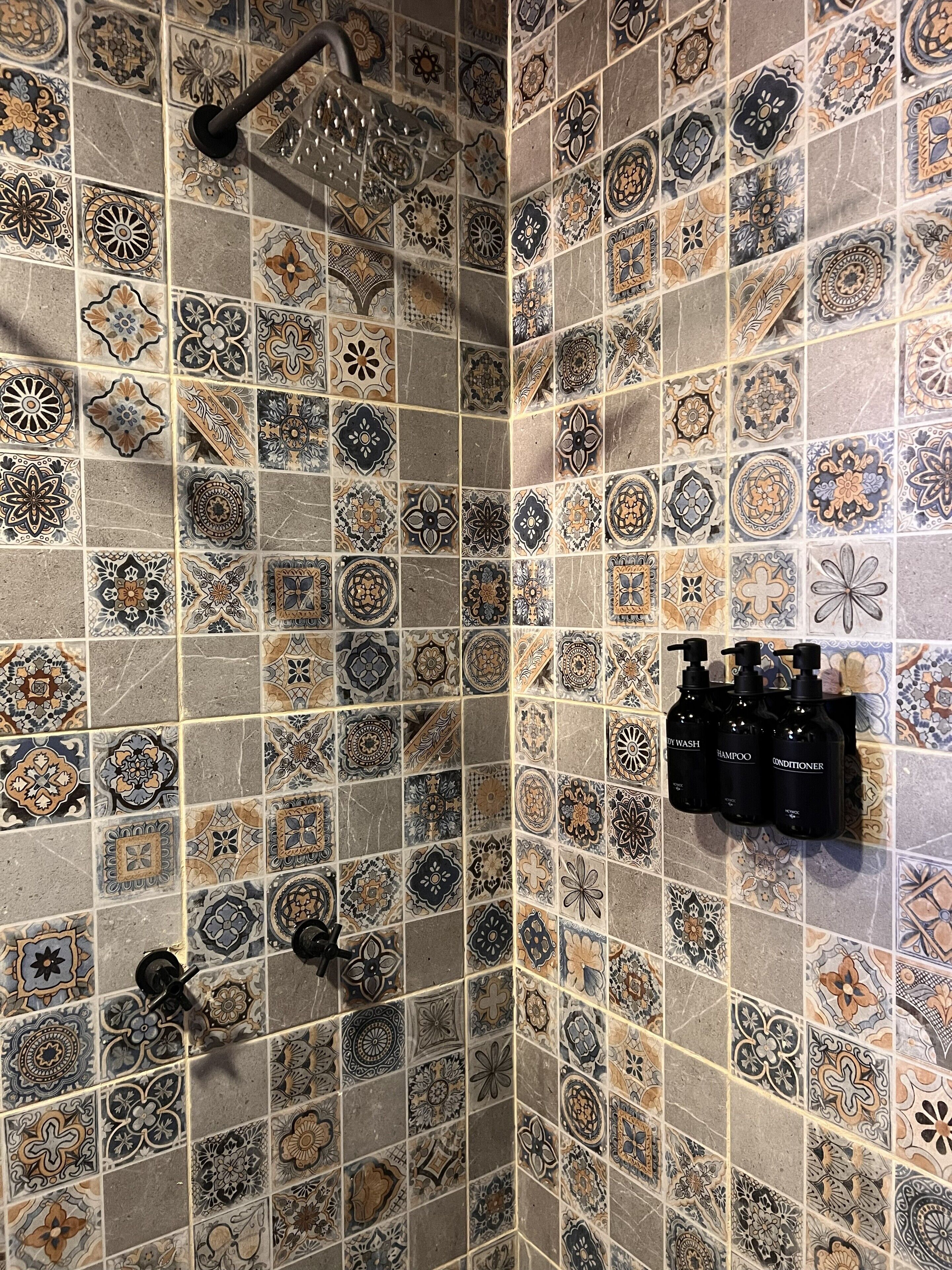 A shower area with ornate tile patterns and black shampoo bottles on a wall.