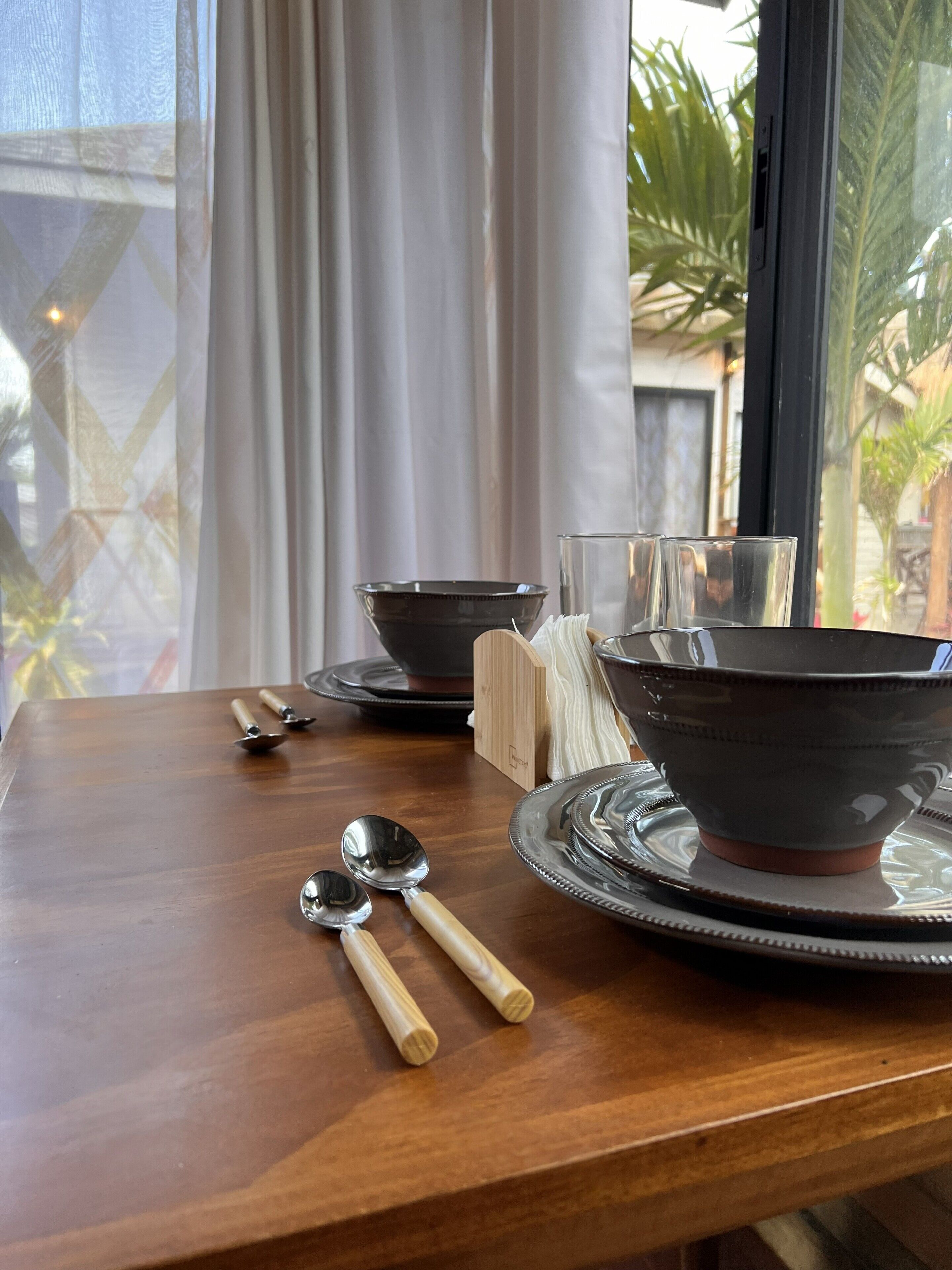 A dining table with a set of bowls, spoons, and a napkin holder.