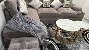 A sectional sofa with multiple cushions, a grey throw blanket, and a round coffee table with gold legs. - Charming 1-bedroom apartment in vibrant Nairobi with fitness room (Nairobi)