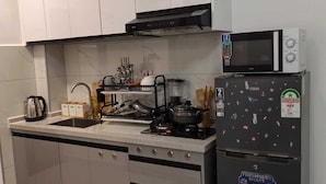 A modern kitchen with white cabinets, a black microwave, a refrigerator with stickers, and a sink with various utensils. - Charming 1-bedroom apartment in vibrant Nairobi with fitness room (Nairobi)