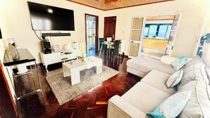 Uma sala de estar com televisão de tela plana, sofá, mesa de centro e espaço para refeições.