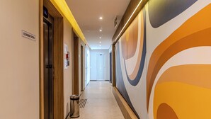 A hallway with an elevator, a trash can, and a wall with abstract art. - Update  (São Paulo)