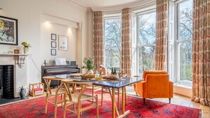 A dining area with a piano, a table with chairs, and a window with curtains. - The Classic on the Mount -  a premium stay that sleeps 4 guests  in 2 bedrooms (York)