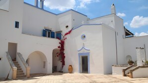Ein weißes Gebäude mit einem Glockenturm, Rundbogenöffnungen und einer Treppe, die zu einer oberen Ebene führt.