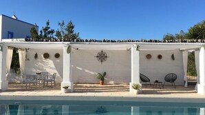 Ein Poolbereich mit überdachter Sitzgelegenheit, einem Pool und einem weißen Geb äude mit blauen Akzenten.