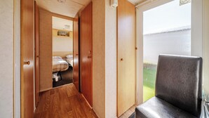 A narrow hallway with wooden flooring, a bed with a white and brown checkered bedspread, and a black chair by a sliding glass door leading to a balcony. - Cayton Bay Caravan for 6, Pet Friendly & Parking (Scarborough)