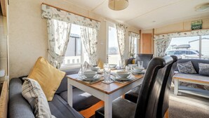 A cozy interior with a dining table set for four, a sofa with cushions, and curtains on the windows. - Cayton Bay Caravan for 6, Pet Friendly & Parking (Scarborough)