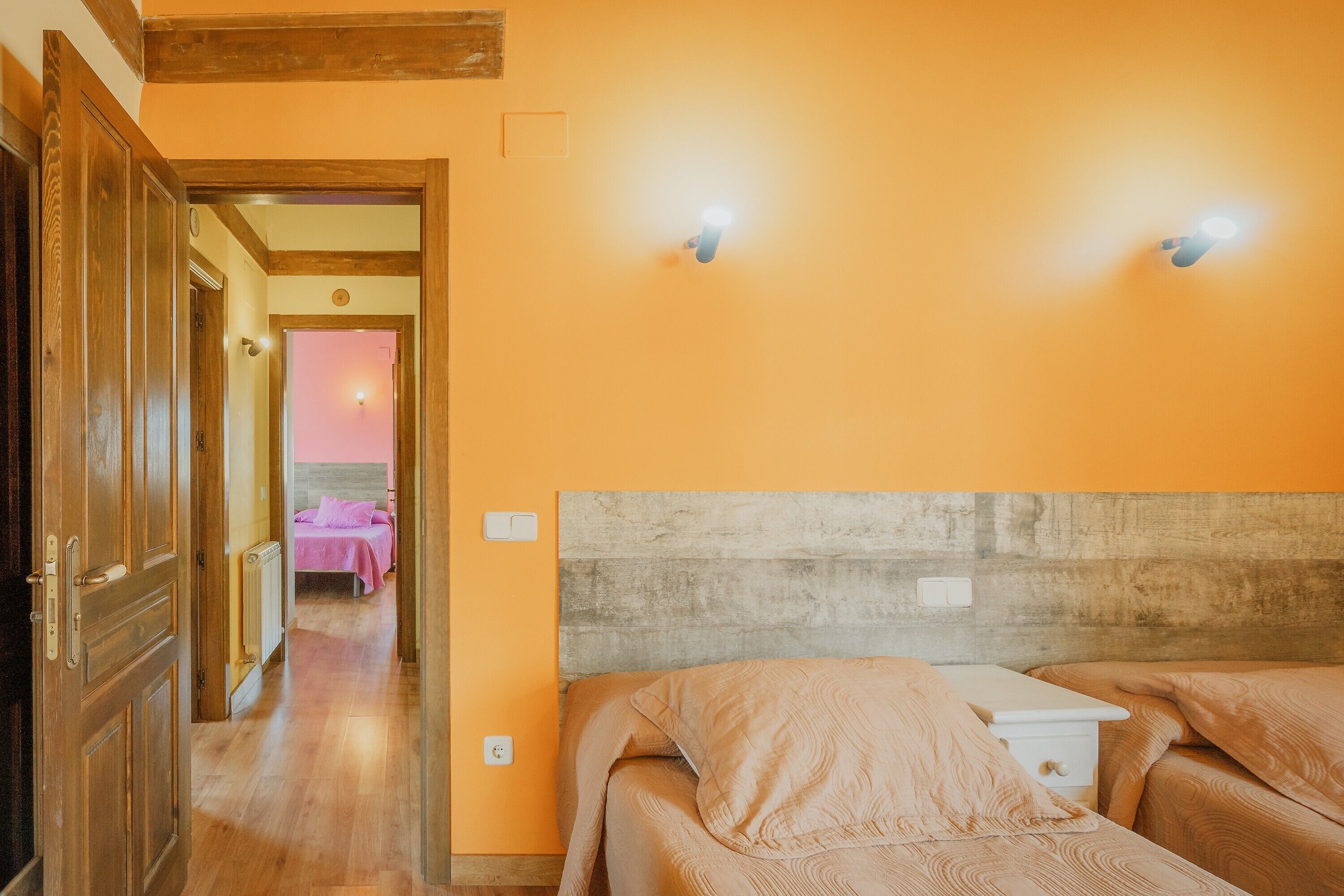 Een hotelkamer met houten vloeren, een bed met een houten hoofdeinde en twee wandlampen.