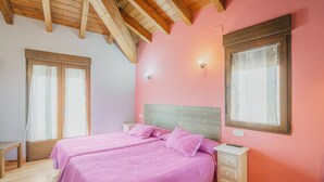 A bedroom with two beds, wooden ceiling beams, a bedside table, and a window with curtains. - Las Eras III Rural House in Medieval Ayllón – 4 Bedrooms with Bathrooms and Mountain Views (Ayllón)
