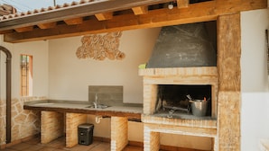 An outdoor kitchen with a stone wall, a brick oven, and a wooden pergola. - Las Eras III Rural House in Medieval Ayllón – 4 Bedrooms with Bathrooms and Mountain Views (Ayllón)