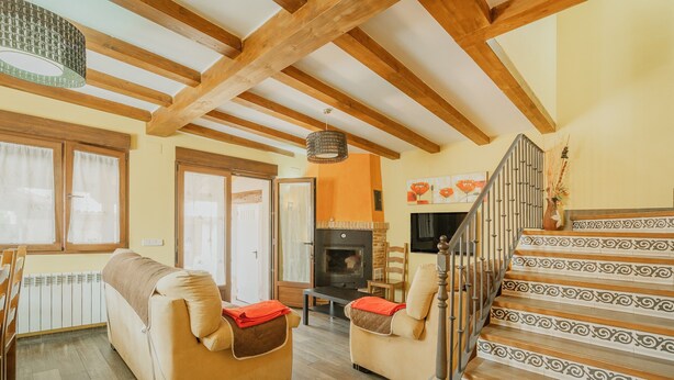 A living room with a sofa, a fireplace, a staircase with patterned steps, and a wooden ceiling. - Las Eras III Rural House in Medieval Ayllón – 4 Bedrooms with Bathrooms and Mountain Views (Ayllón)