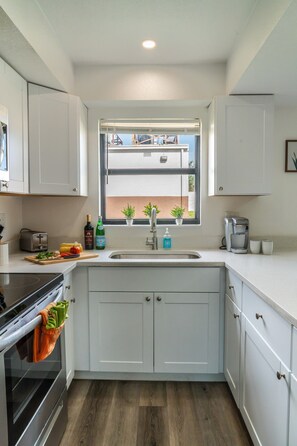 A modern kitchen with white cabinets, a built-in oven, a window with potted plants, and a coffee maker. - Modern Coral Gem: Patio | Work Space | Downtown (Cape Coral)