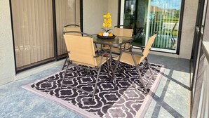 A patio with a table and chairs, a patterned rug, and a sliding glass door leading to a backyard. - Modern Coral Gem: Patio | Work Space | Downtown (Cape Coral)