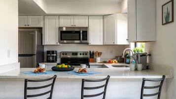 A modern kitchen with white cabinets, a stainless steel microwave, a built-in oven, and a large island with bar stools.
