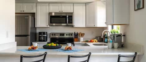Una cocina moderna con armarios blancos, un microondas de acero inoxidable, un horno empotrado y una isla grande con taburetes de bar.