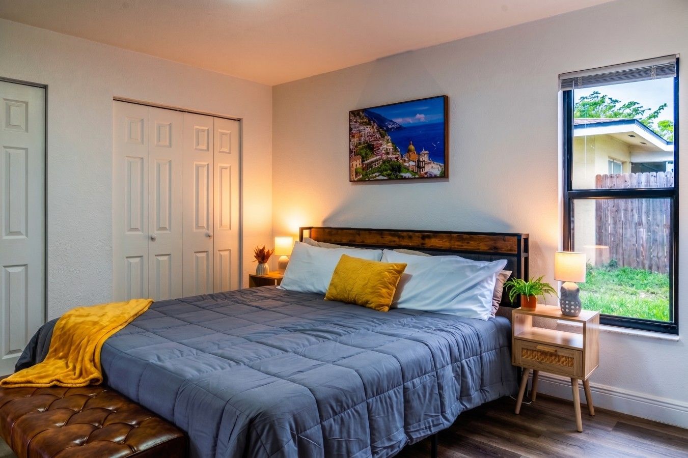 A bedroom with a bed, bedside tables, a window with a view, and a door.