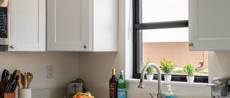 Una cocina moderna con armarios blancos, horno empotrado, lavamanos y ventana con plantas en macetas.