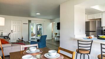 Una cocina moderna con electrodomésticos de acero inoxidable, un comedor con mesa de madera para cuatro personas y una sala de estar con un sillón azul.