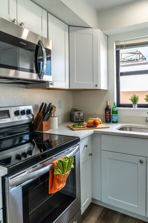 Een moderne keuken met witte kasten, een roestvrijstalen fornuis, een magnetron en een raam met uitzicht.