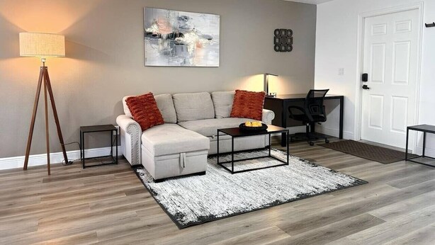 A modern living room with a sofa, coffee table, and a lamp. - Modern Coral Gem: Patio | Work Space | Downtown (Cape Coral)