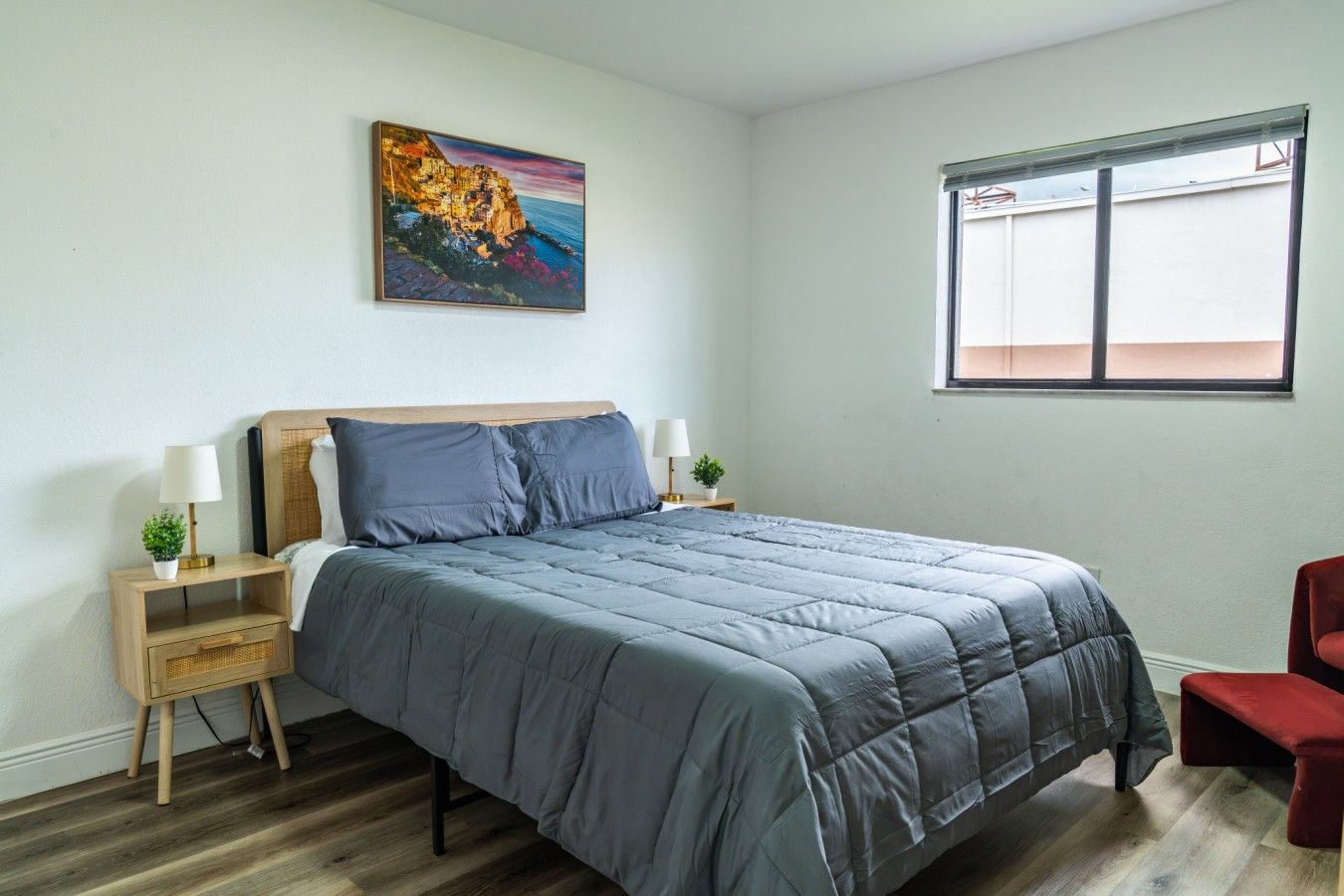 A bedroom with a bed, nightstands, a window, and a painting.