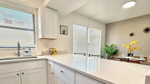 A kitchen with white cabinets, a countertop, and a window with blinds. - Modern Coral Gem: Patio | Work Space | Downtown (Cape Coral)