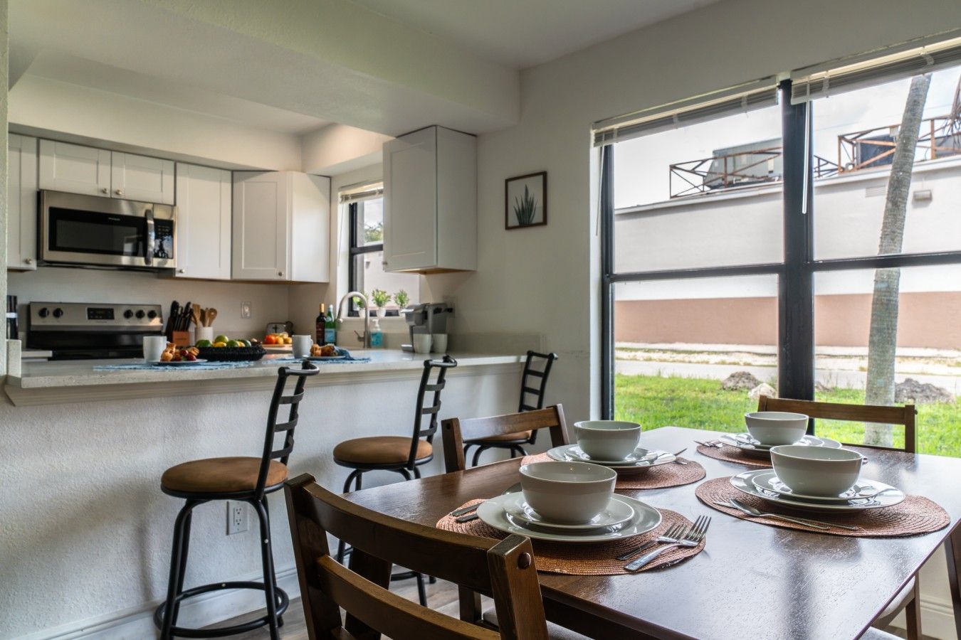 Une cuisine moderne avec des armoires blanches, un four à micro-ondes encastré et un coin repas avec une table dressée pour quatre personnes.