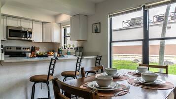 Una cocina moderna con armarios blancos, un microondas integrado y un comedor con una mesa lista para cuatro comensales.