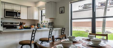 Une cuisine moderne avec des armoires blanches, un four à micro-ondes encastré et un coin repas avec une table dressée pour quatre personnes.