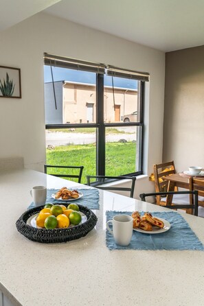 A dining area with a table set for two, featuring a plate of pastries and a bowl of fruit. - Modern Coral Gem: Patio | Work Space | Downtown (Cape Coral)