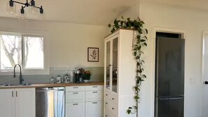 Eine Küche mit weißen Schränken, einem Edelstahl-Kühlschrank, einem Geschirrspüler und einem Fenster mit Blick auf Bäume.