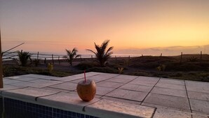 Une vue sur la piscine avec un coucher de soleil, une boisson à la noix de coco et une clôture.