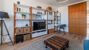 Una sala moderna con televisión, estanterías, una lámpara y un sofá azul.
