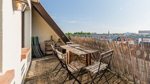 Un balcón con mesa y sillas de madera, vista panorámica de la ciudad y una barandilla.